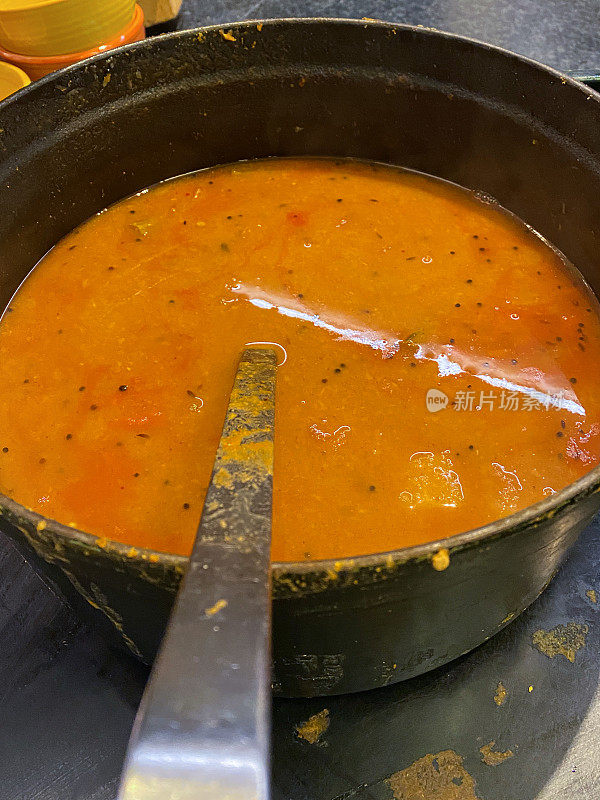 特写图像的印度早餐食谱sambar(辣扁豆和蔬菜炖)在金属碗与勺子，masoor dal(红扁豆)，tul dal(鸽子豌豆)，番茄，胡萝卜，洋葱和秋葵，高架视图